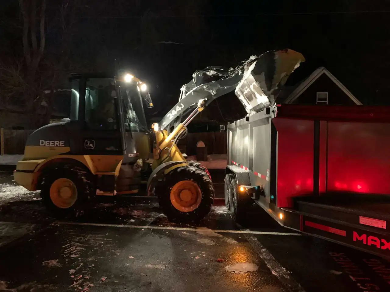 Crystal Clear loader dumping snow into a trailer at night for hauling