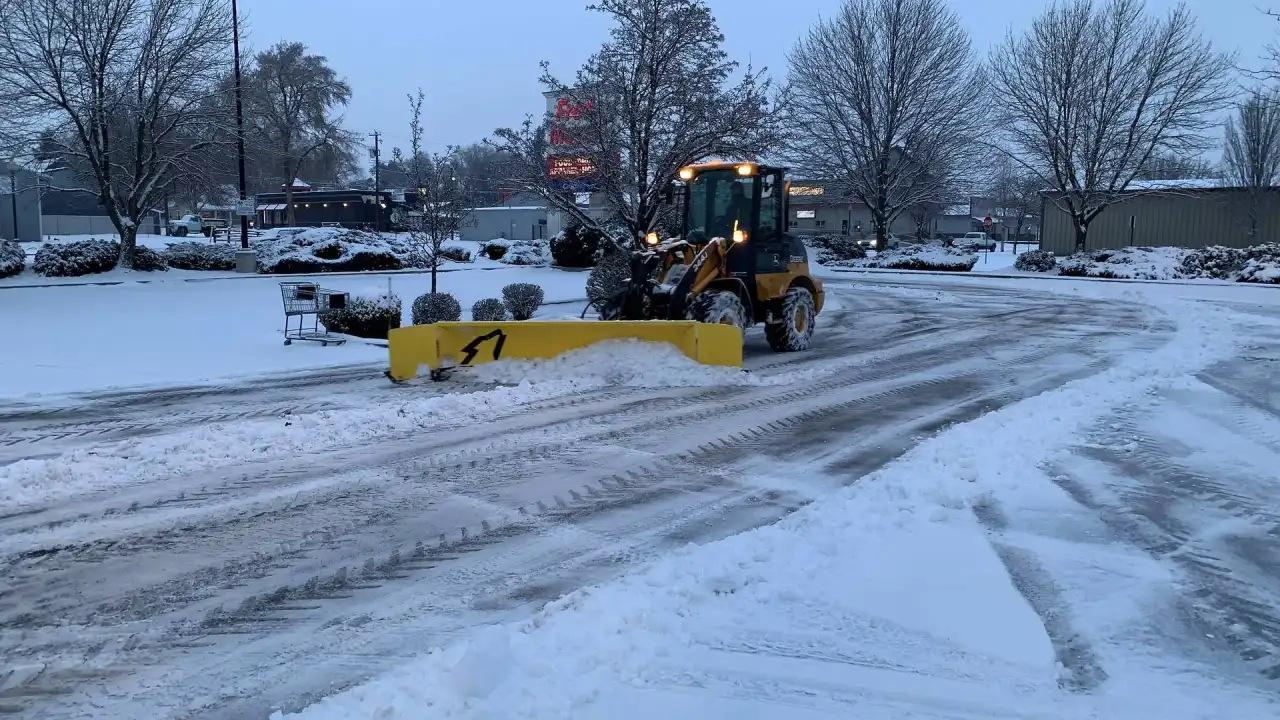 Crystal Clear loader with a yellow snow pusher clearing a commercial parking lot
