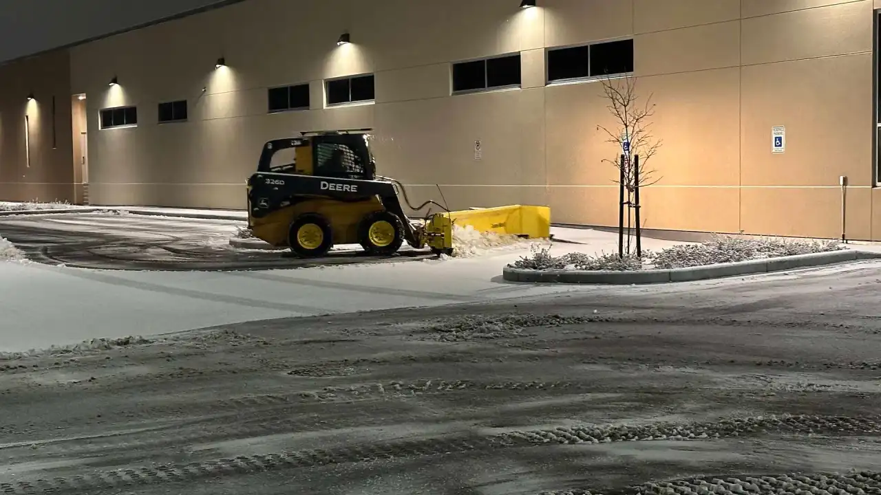 Crystal Clear skid steer plowing beside a commercial building at night